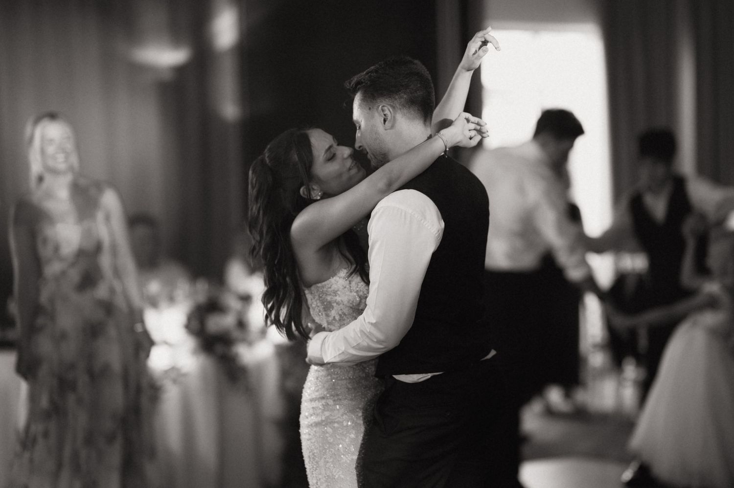 Black and white photo of a bride and groom sharing their first dance at a wedding reception.