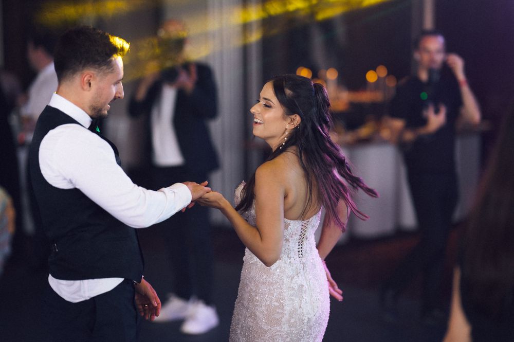 Bride and groom share their first dance at wedding reception, woman in lace gown with purple hair highlights.