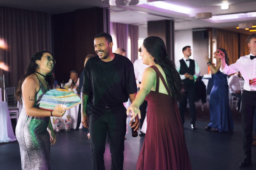 People dancing and laughing at an elegant event, wearing formal attire in a decorated venue.