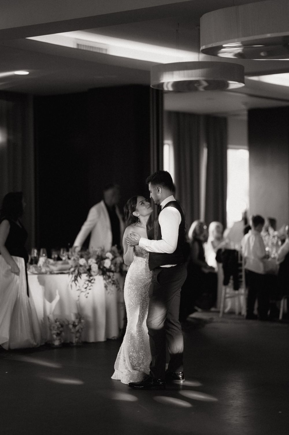 Black and white photo of a bride and groom sharing their first dance at a wedding reception.