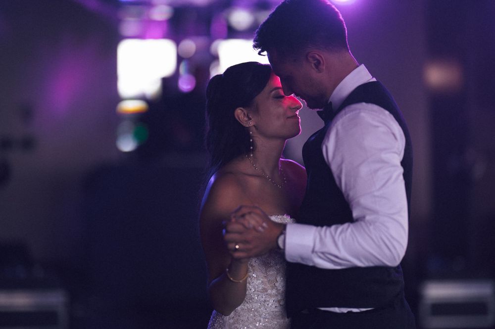 Bride and groom share an intimate first dance, embracing under purple wedding reception lights.