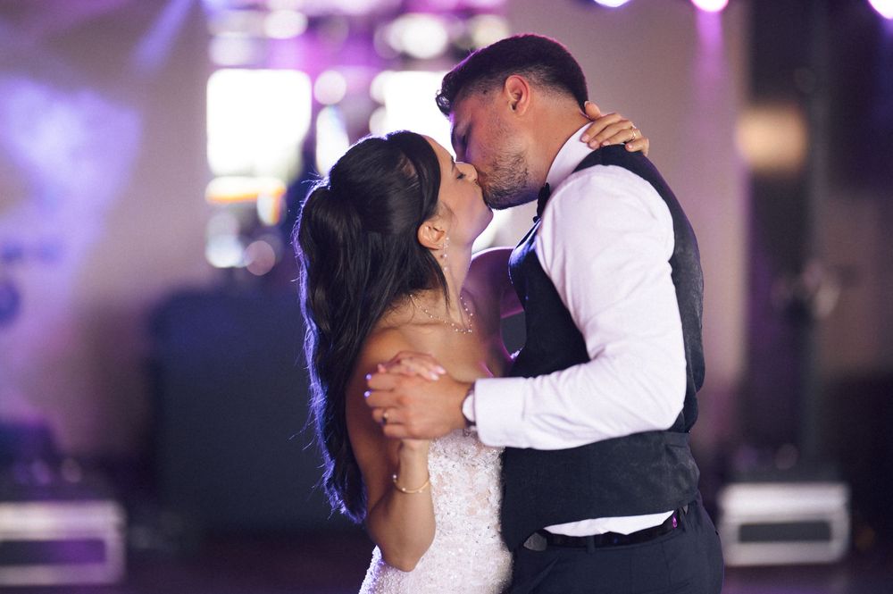 Bride and groom share a romantic first dance kiss at their wedding reception with purple lighting.
