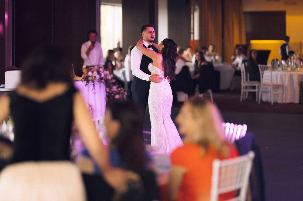 Bride and groom share their first dance at elegant wedding reception with guests seated at decorated tables.