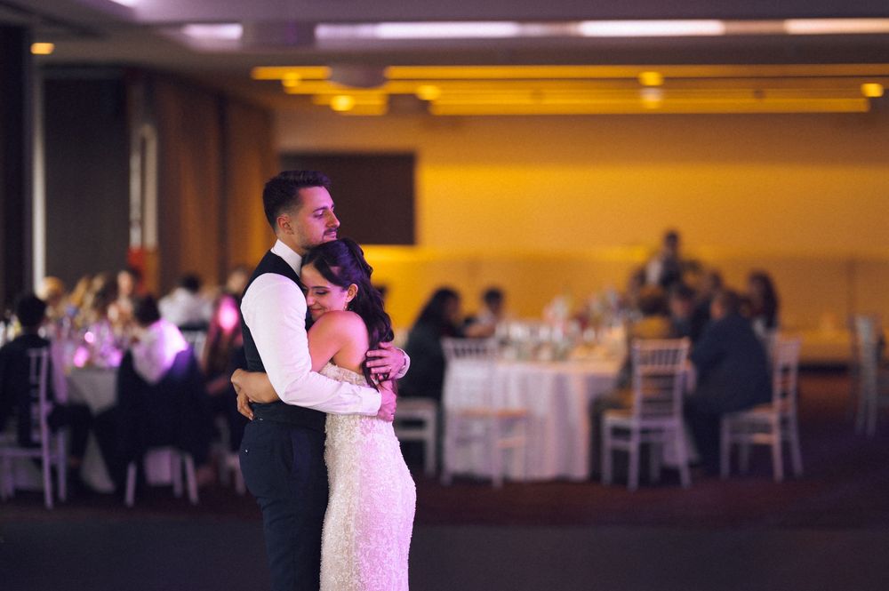 Bride and groom share their first dance at an elegant wedding reception with guests seated at decorated tables.
