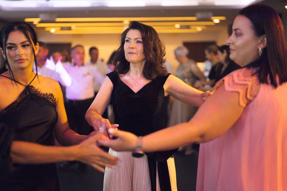 Women in elegant attire holding hands while dancing together at a formal event or celebration.