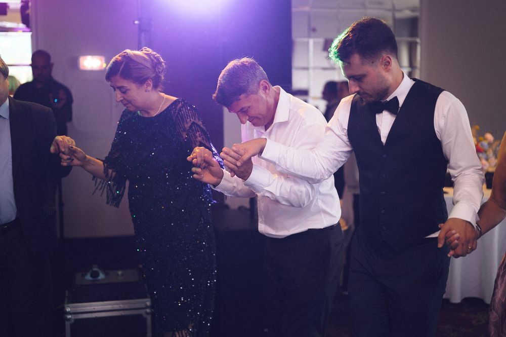 Three guests dancing together at a wedding reception in formal attire under purple lighting.