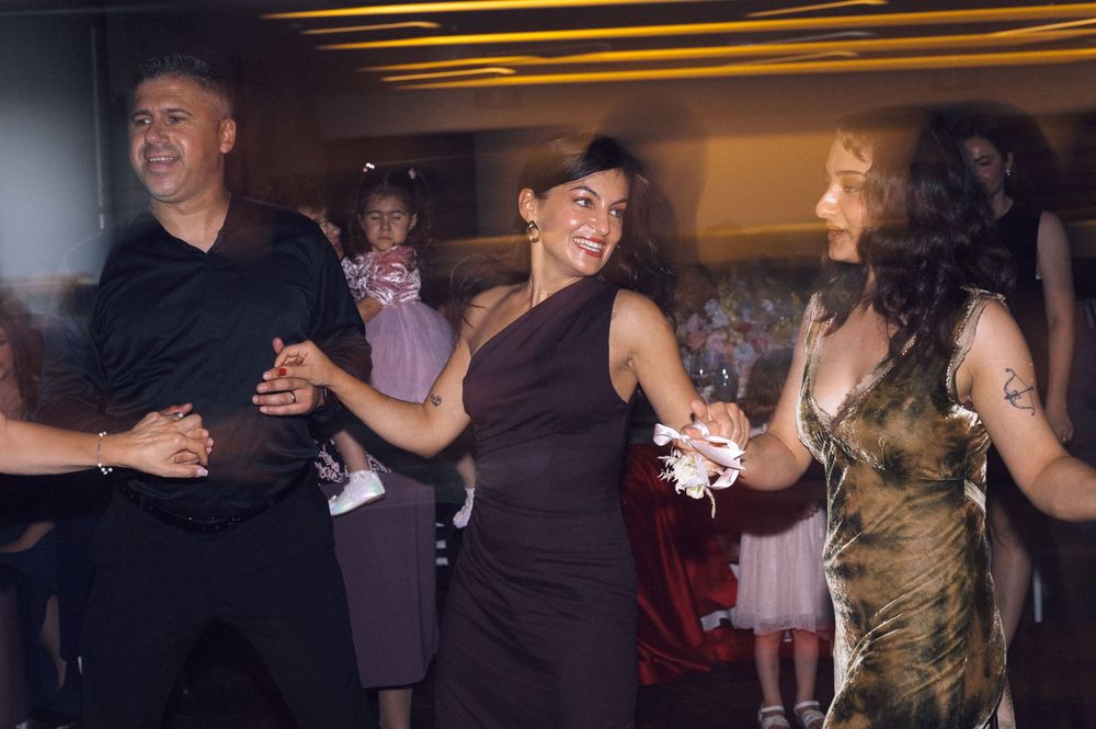 Group of people dancing joyfully at a party, wearing elegant dark outfits under warm ambient lighting.