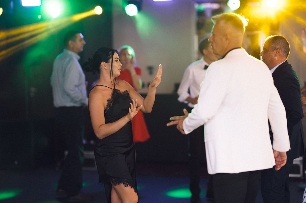 Couple dancing at a nightclub event with colorful stage lights and guests in formal attire in the background.