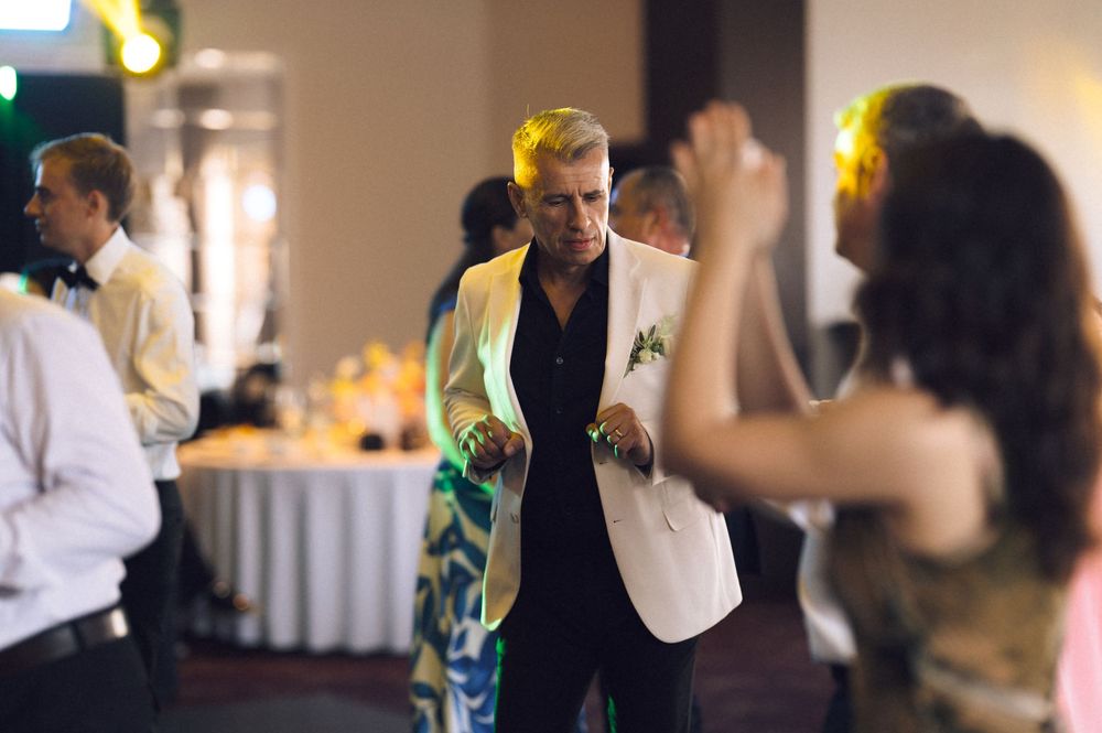 Guests dancing at an elegant wedding reception in a banquet hall, man in white blazer dancing with woman.