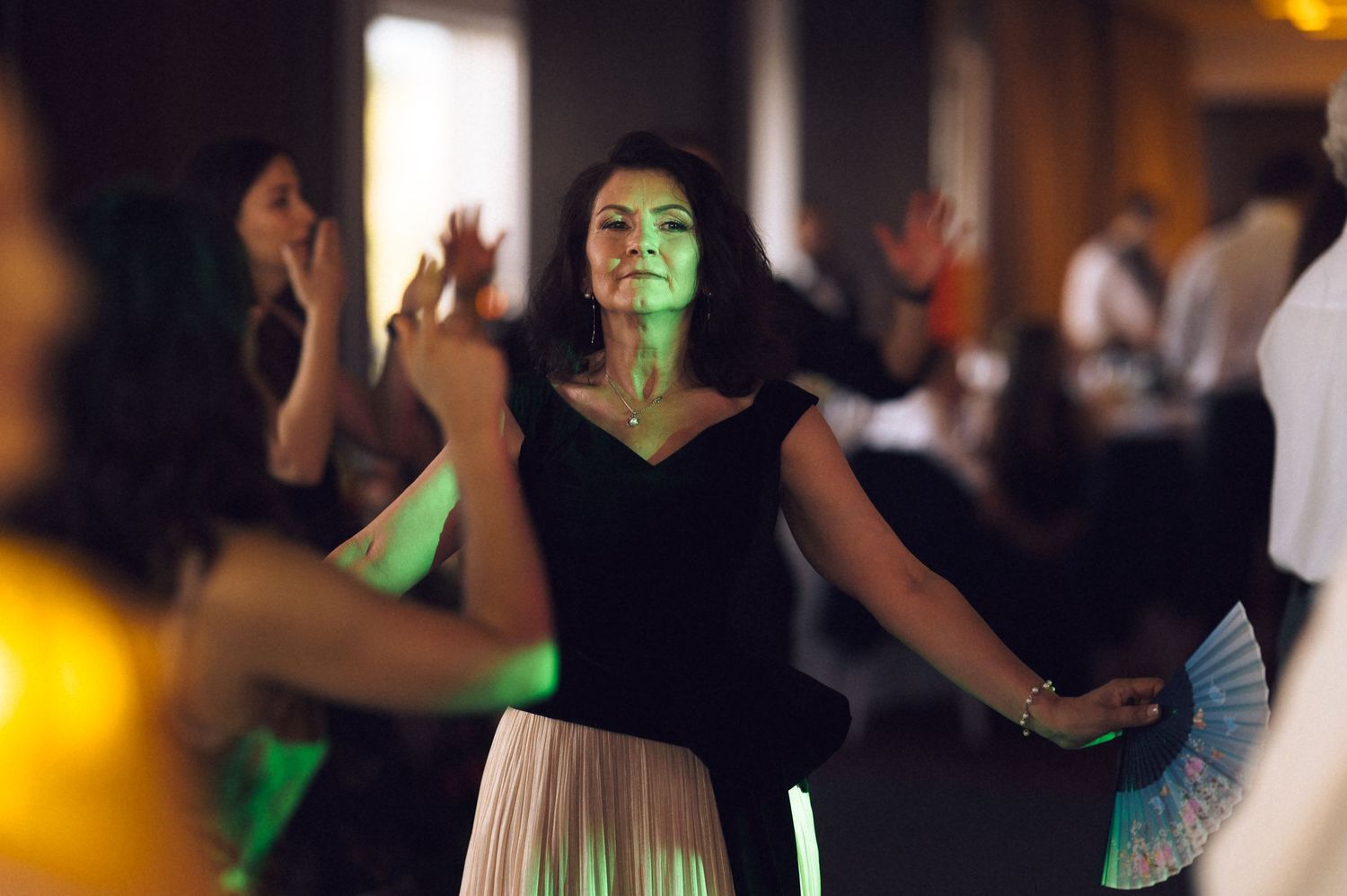 Woman in black top and white skirt dancing at an elegant event with colorful green lighting.