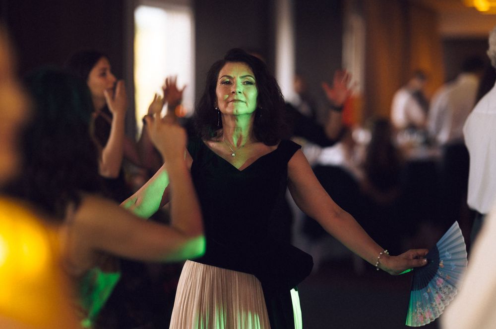 Woman in black top and white skirt dancing at an elegant event with colorful green lighting.