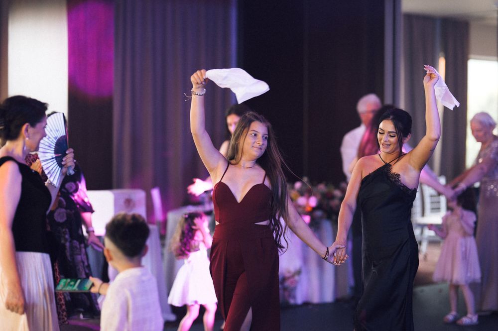 Two women dancing joyfully at a formal event, waving white napkins in a festive ballroom celebration.