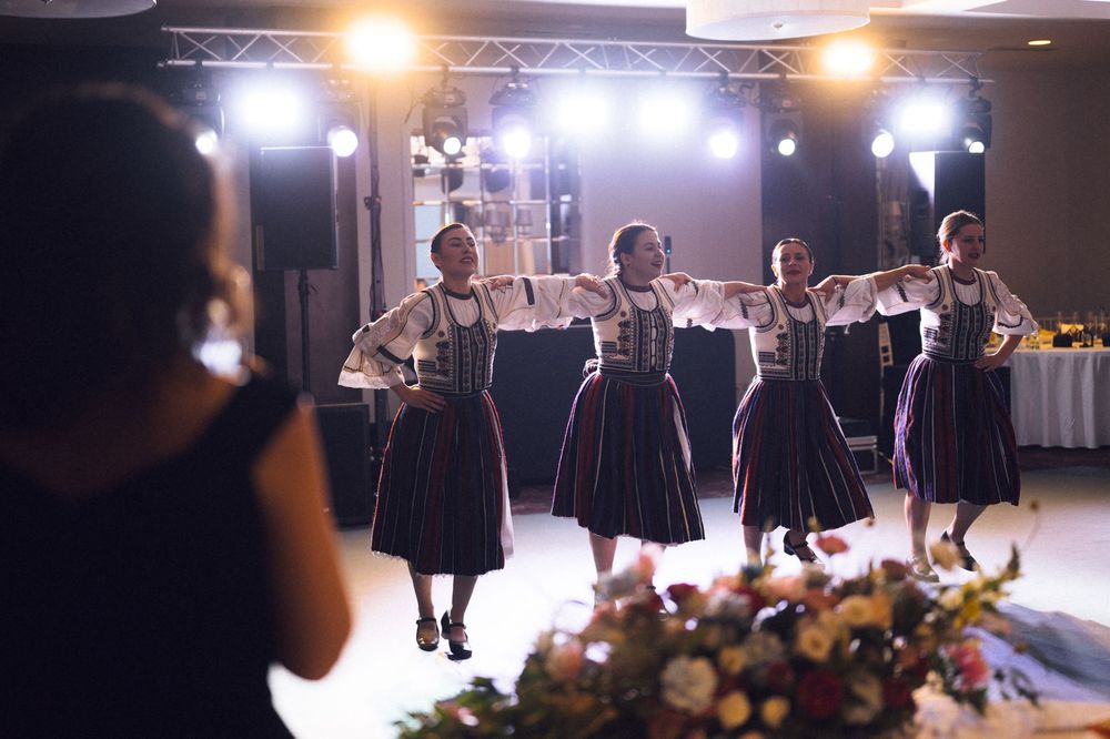 Four women in traditional folk costumes perform a dance routine at an elegant indoor event venue.