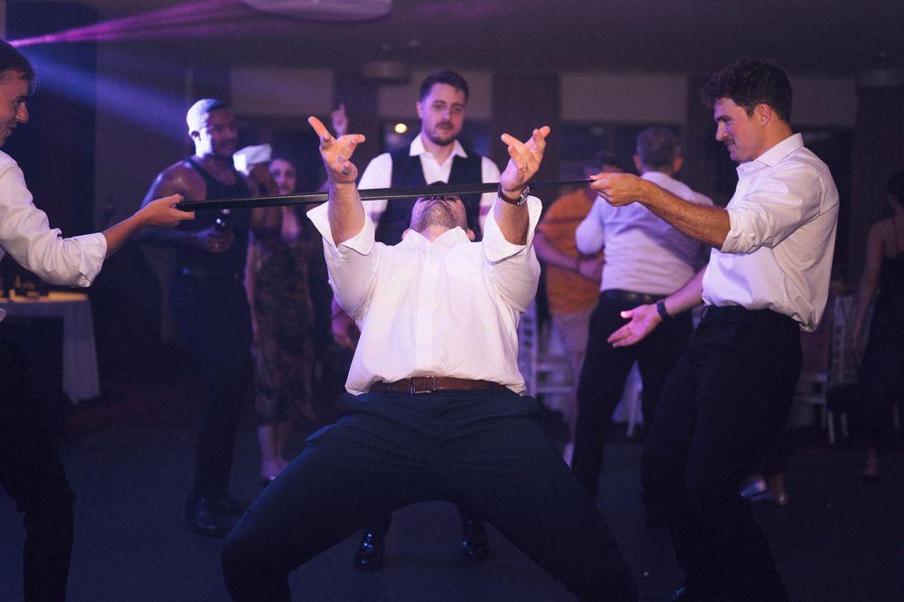 Men dancing energetically at a wedding reception party under colorful lights on the dance floor.