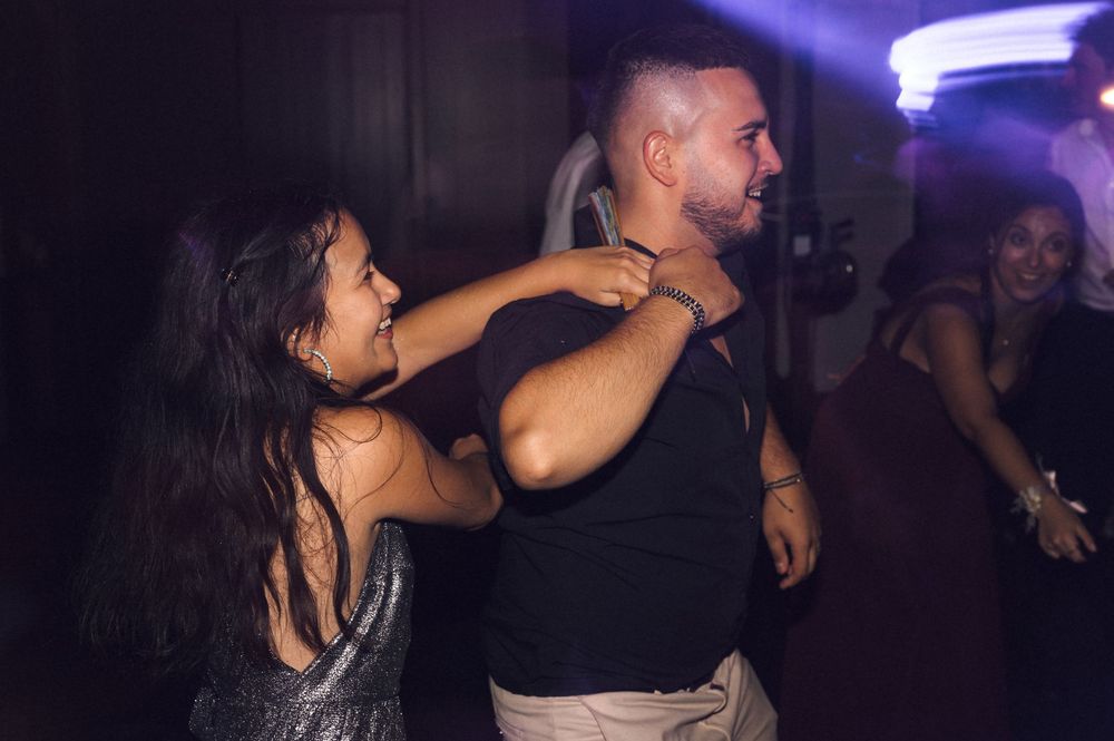 Couple dancing together at a lively party, woman in sparkly dress laughing with man in black shirt.