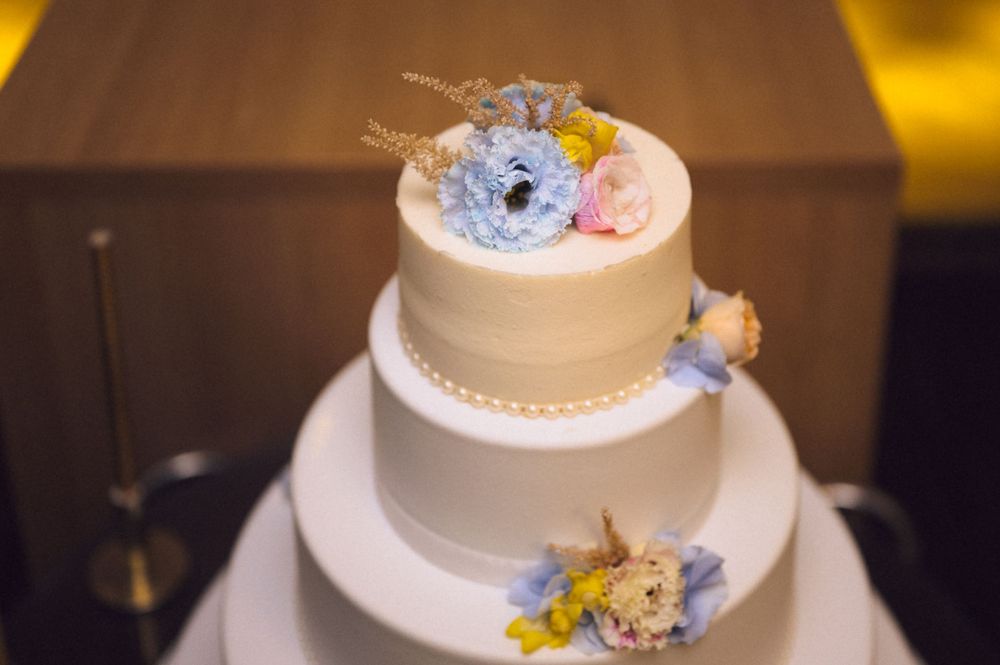 Elegant three-tier white wedding cake topped with blue, pink, and yellow flowers.
