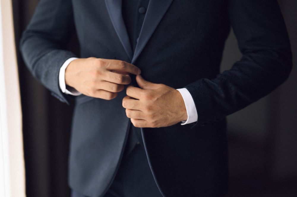 Man in dark navy suit adjusting jacket buttons, showcasing elegant formal menswear fashion.