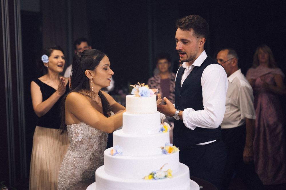 Bride and groom cutting a four-tier white wedding cake decorated with flowers at their wedding reception.