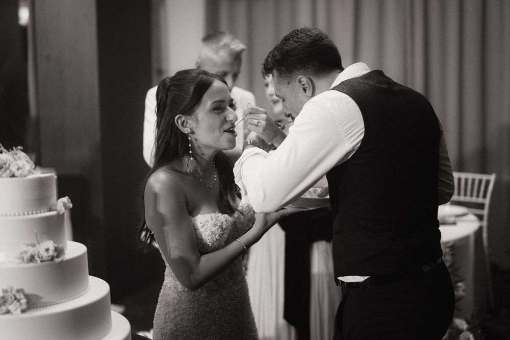 Black and white photo of bride and groom sharing a tender moment while cutting their elegant tiered wedding cake.