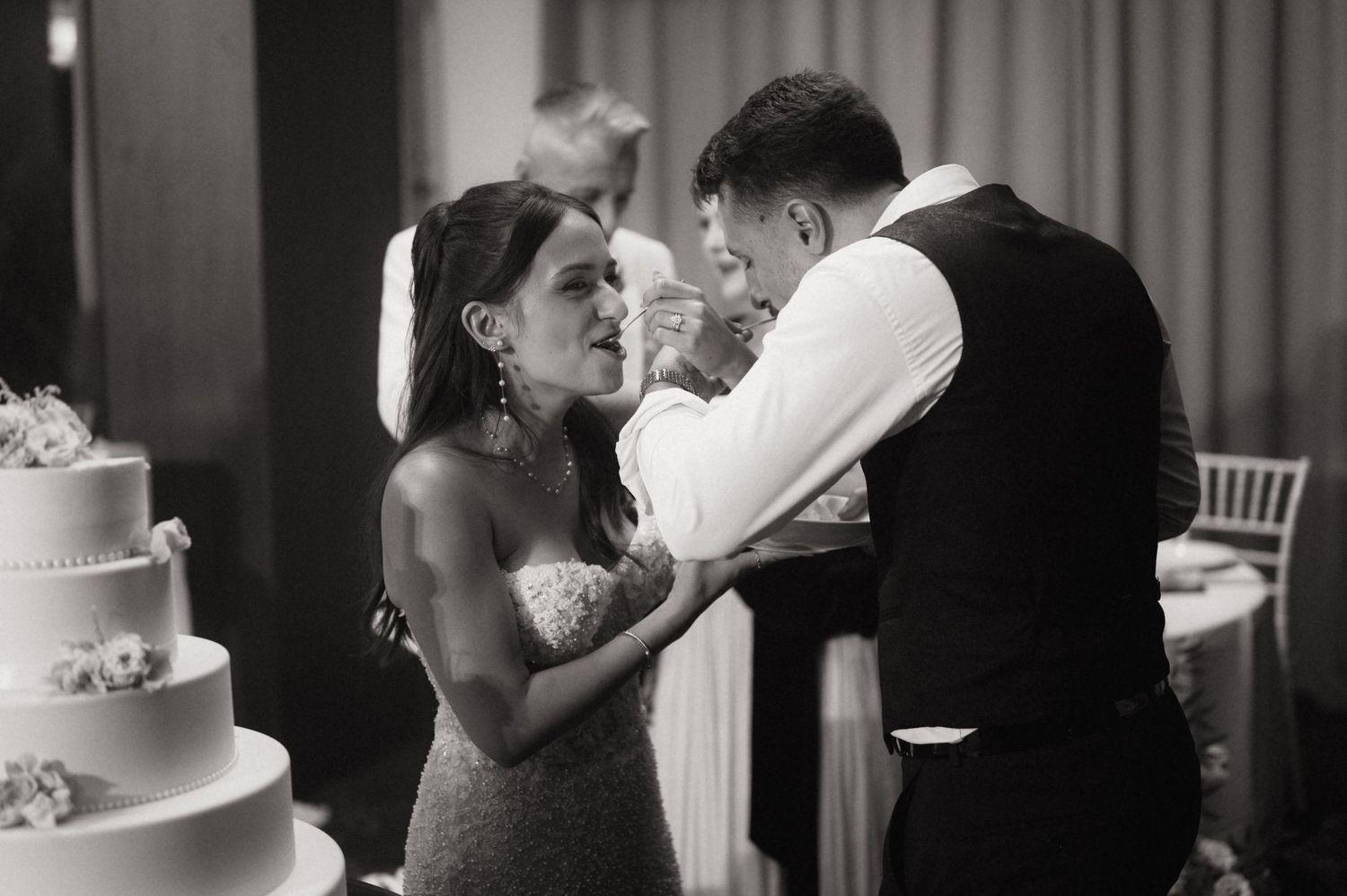 Black and white photo of bride and groom sharing a tender moment while cutting their elegant tiered wedding cake.