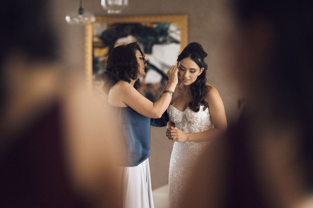 Bridesmaid helping bride with veil adjustments in elegant indoor wedding preparation setting.