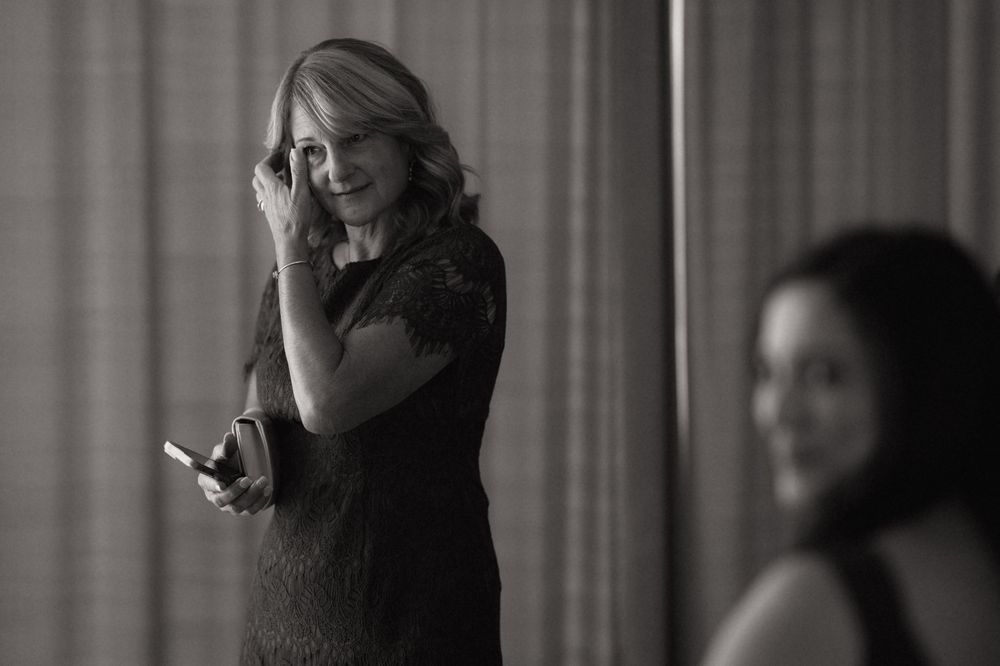 Black and white photo of a woman in a lace dress holding a phone, smiling candidly at an elegant event.