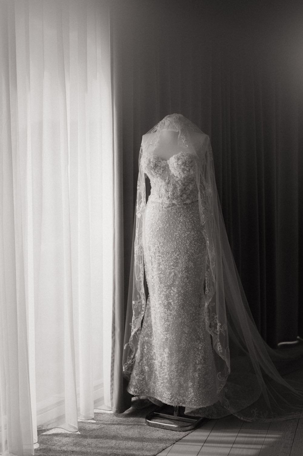 Elegant lace wedding dress with cathedral veil displayed on mannequin in black and white photography.
