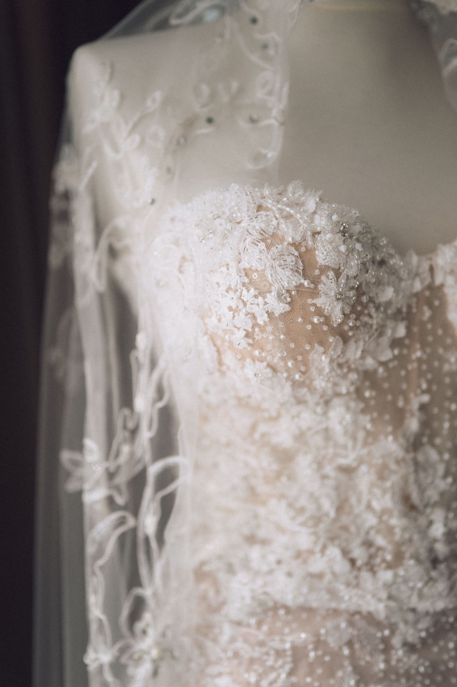 Elegant white lace wedding dress with floral appliques and pearl beading displayed on a mannequin with a flowing veil.