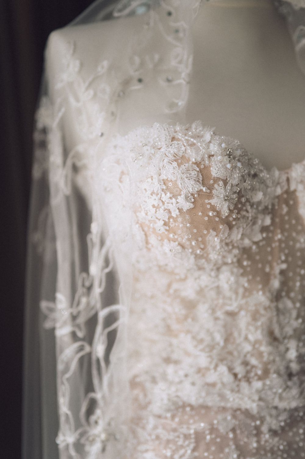 Elegant white lace wedding dress with floral appliques and pearl beading displayed on a mannequin with a flowing veil.