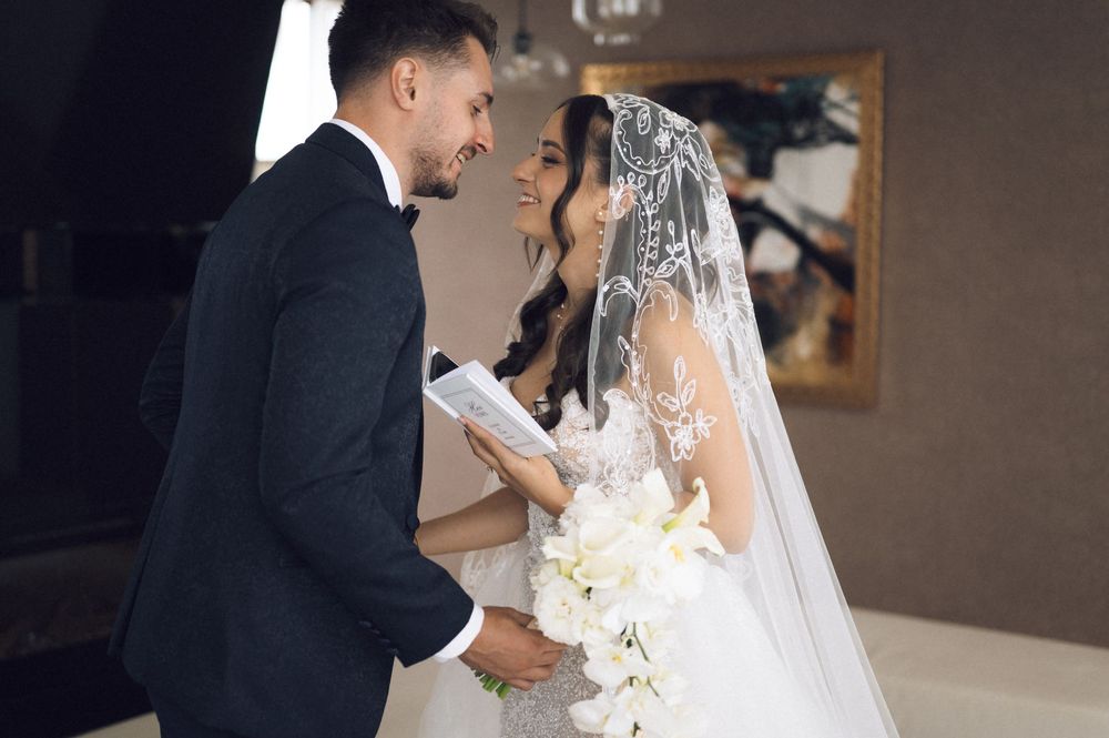 Bride and groom exchanging vows at wedding ceremony, bride holding white floral bouquet wearing lace veil.