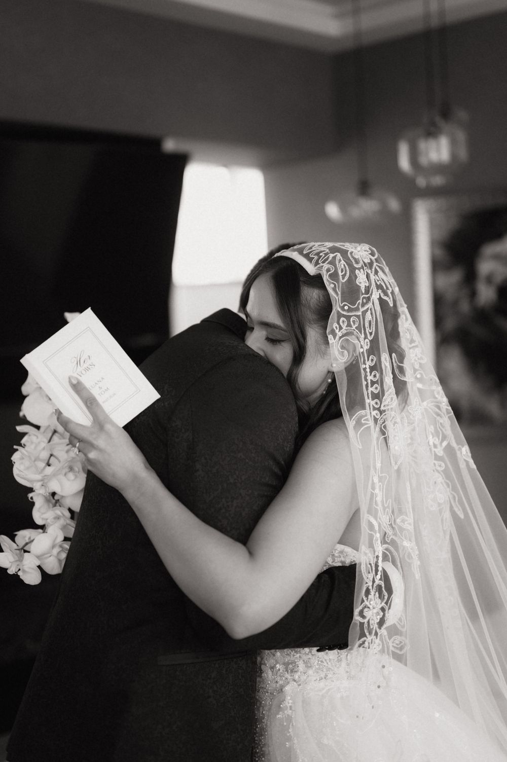 Black and white photo of a bride and groom sharing an emotional hug during their wedding ceremony.