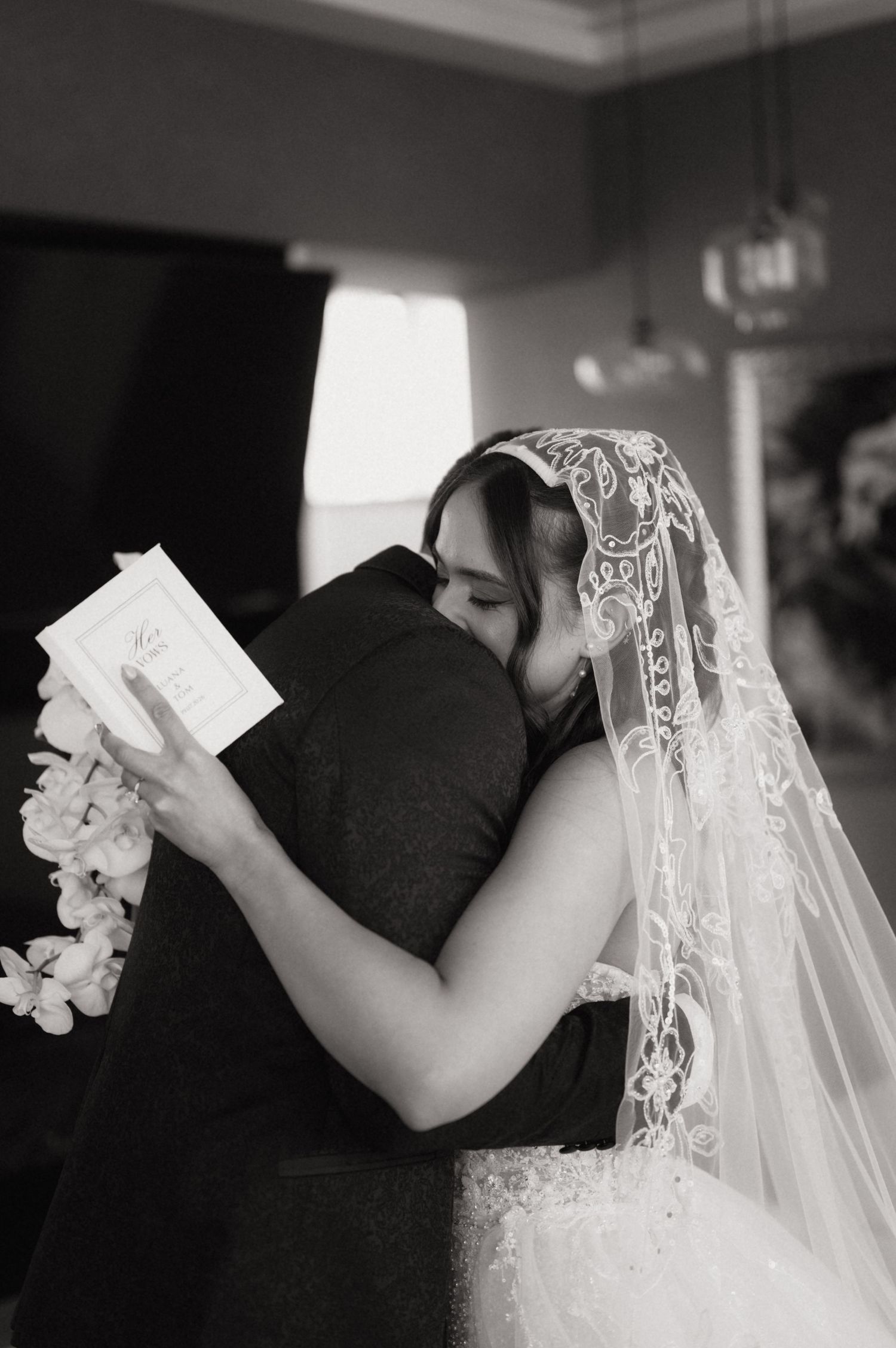 Black and white photo of a bride and groom sharing an emotional hug during their wedding ceremony.
