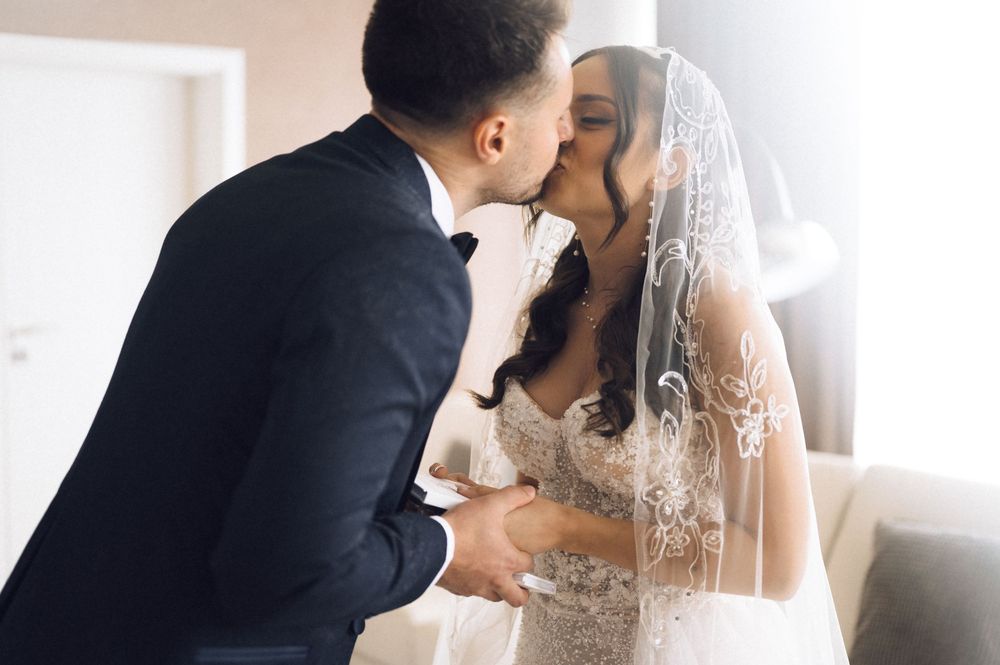 Bride and groom share a romantic kiss, bride wearing lace wedding dress and veil on their wedding day.