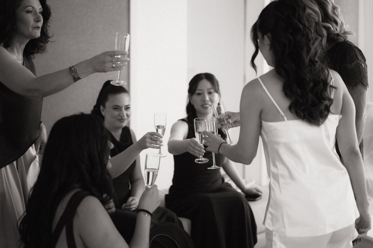 Women toasting with champagne glasses at a wedding celebration in black and white photo.