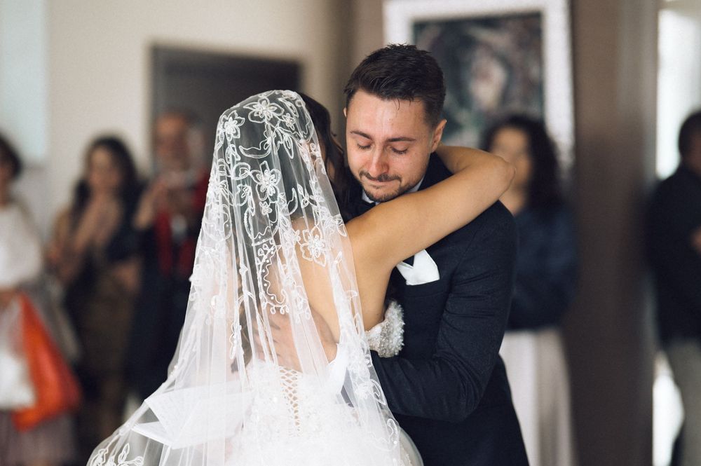 Bride and groom share an emotional first dance embrace, bride wearing lace veil at elegant wedding reception.