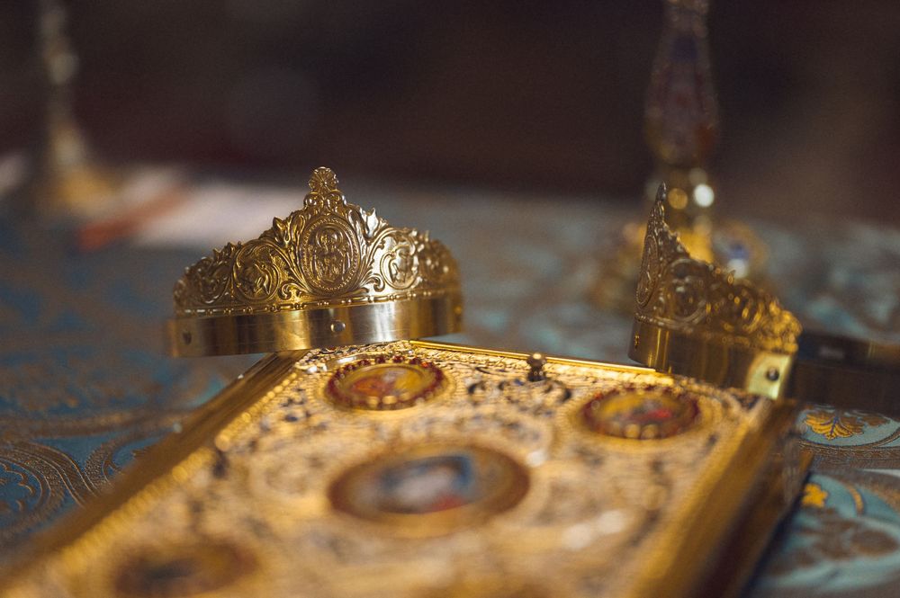 Golden Orthodox wedding crowns resting on an ornate gilded Bible during a traditional religious ceremony.