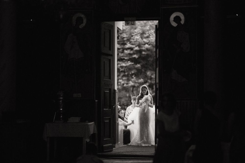 Black and white wedding photo of bride and groom framed in church doorway with icons visible.