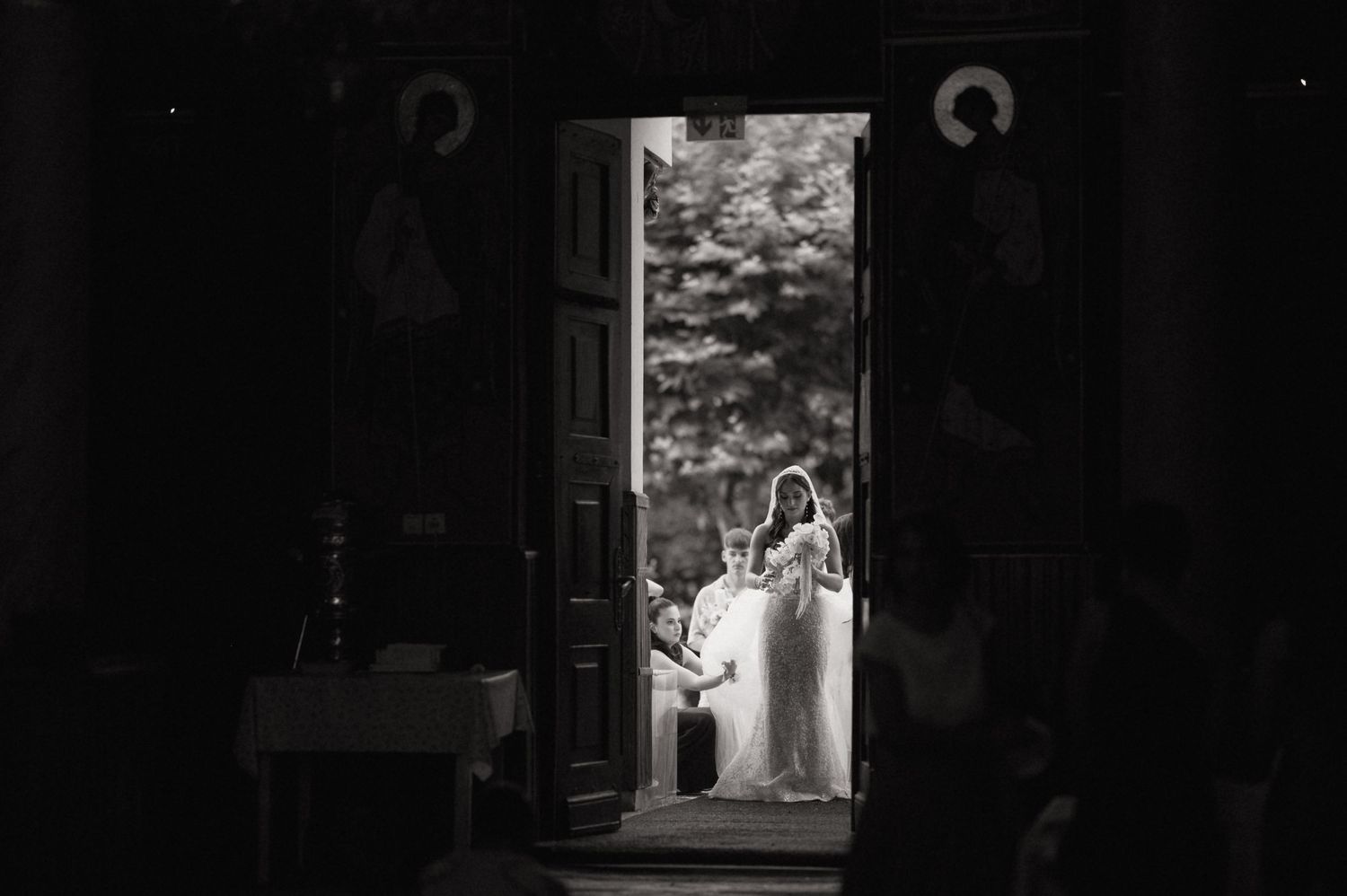 Black and white wedding photo of bride and groom framed in church doorway with icons visible.
