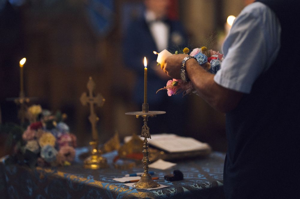 Person lighting candles near a golden cross on a decorated altar during a religious ceremony.
