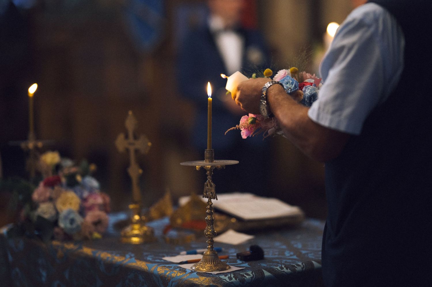 Person lighting candles near a golden cross on a decorated altar during a religious ceremony.