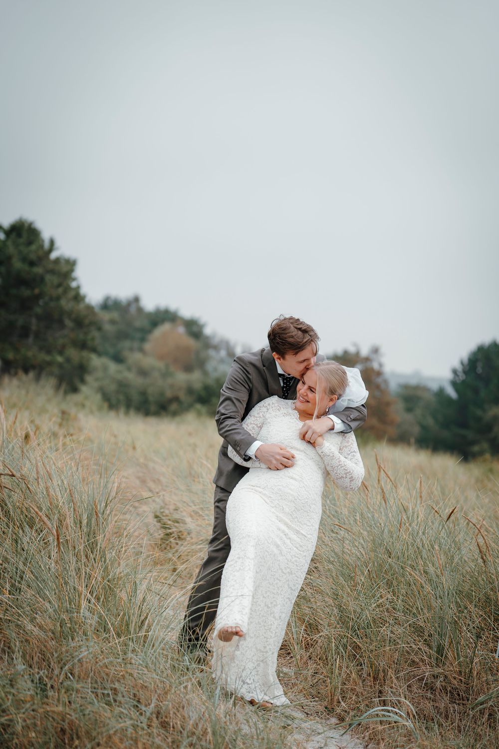 A candid wedding moment captured on a rustic path with tall grass, showing playful interaction between newlyweds.