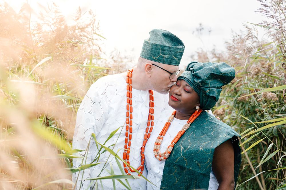 Couple wearing traditional white and green ceremonial clothing embracing outdoors.