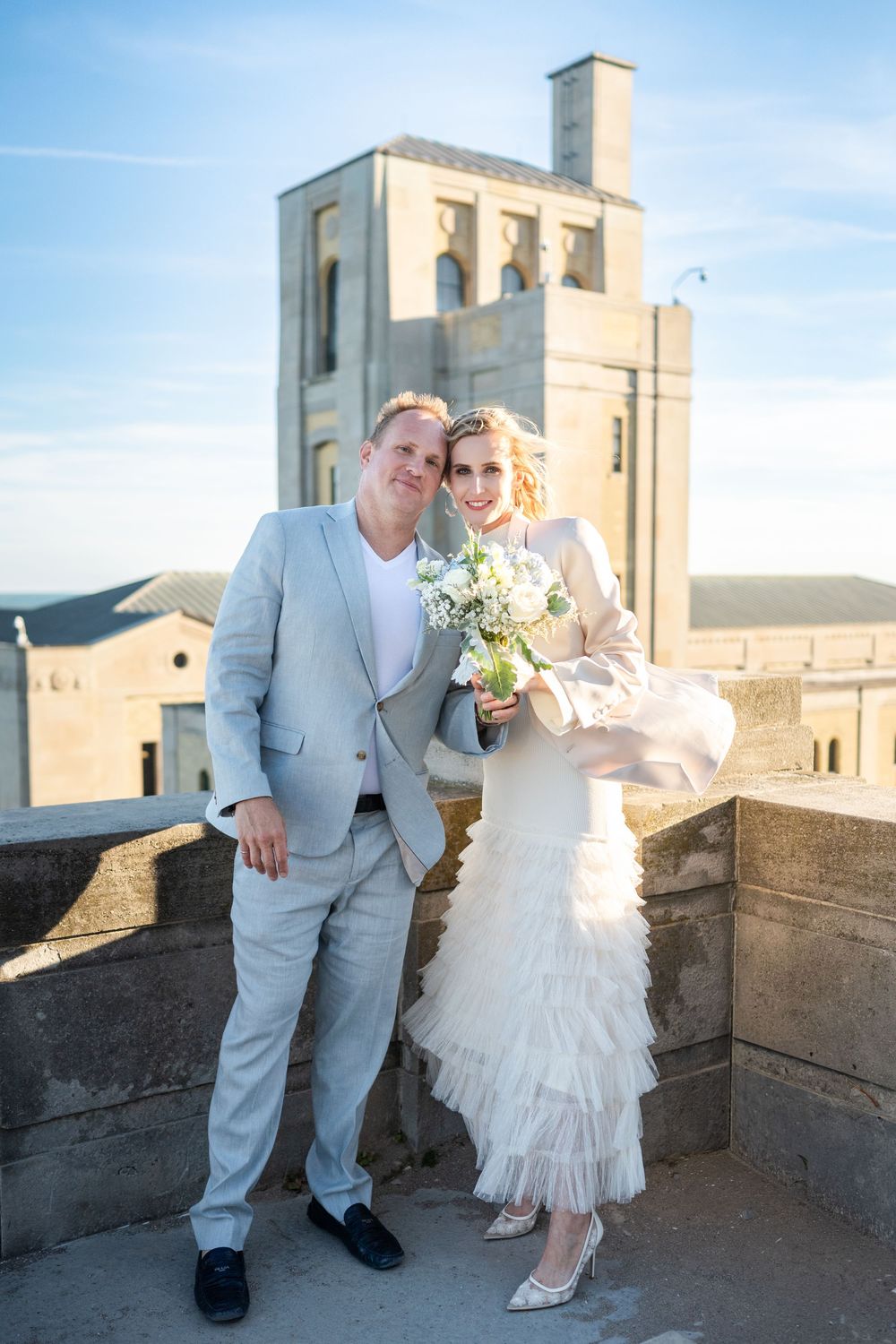 Bride and groom on a rooftop terrace with a historic stone tower rising behind them.