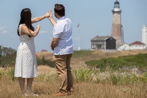 Engaged couple sharing a joyful moment together with a scenic lighthouse in the background.