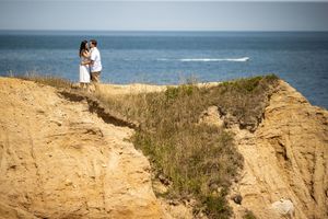 Romantic couple embracing on dramatic coastal cliffs overlooking the deep blue ocean.