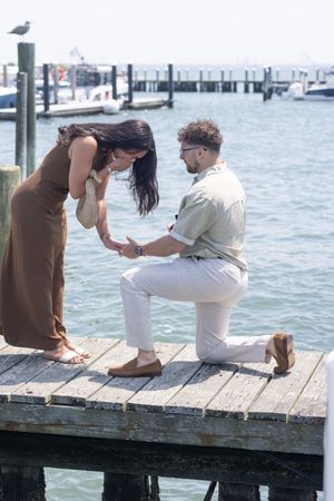Couple sharing an emotional engagement moment on a weathered dock surrounded by harbor waters.