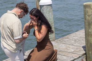 Emotional woman crying tears of joy during a surprise marriage proposal on a sunny harbor dock.