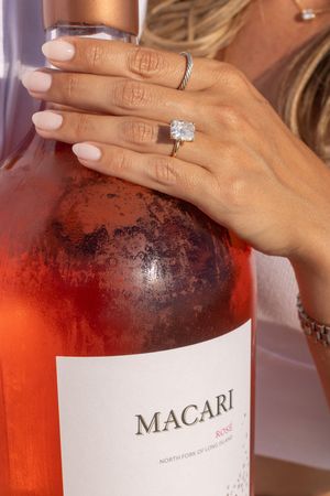 Close-up of an engagement ring on a hand resting on a Macari Rosé wine bottle.
