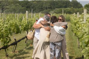 Group of people sharing warm hugs and celebrating together among vineyard rows outdoors.