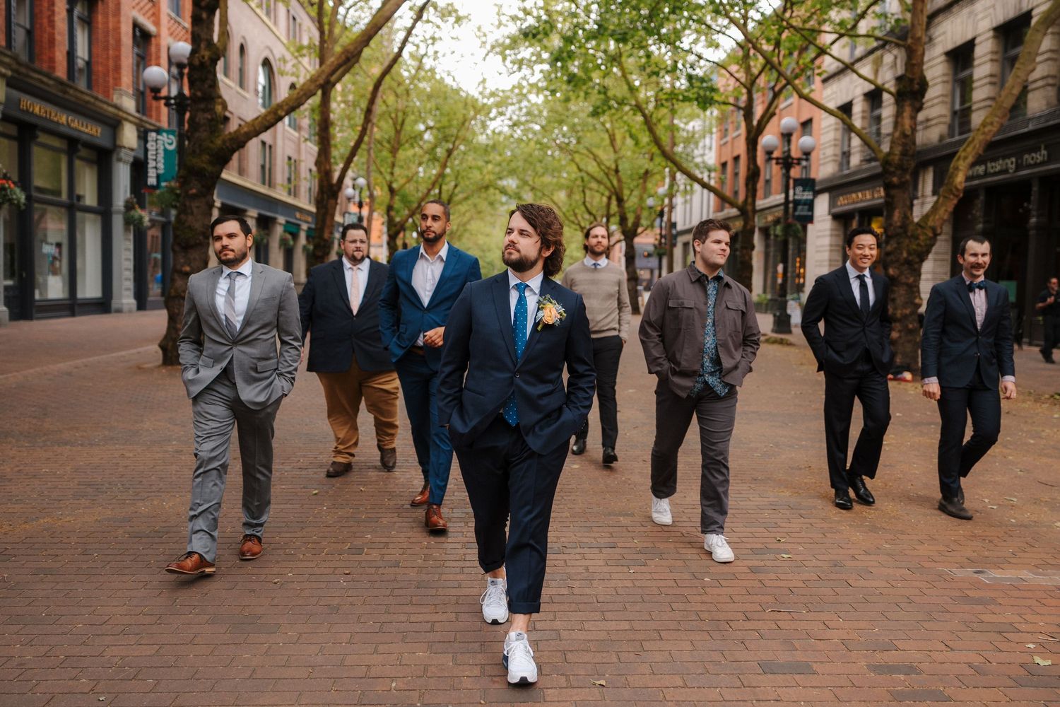Ryker in navy suit leads groomsmen walking on a bricks at their 210 pioneer square wedding